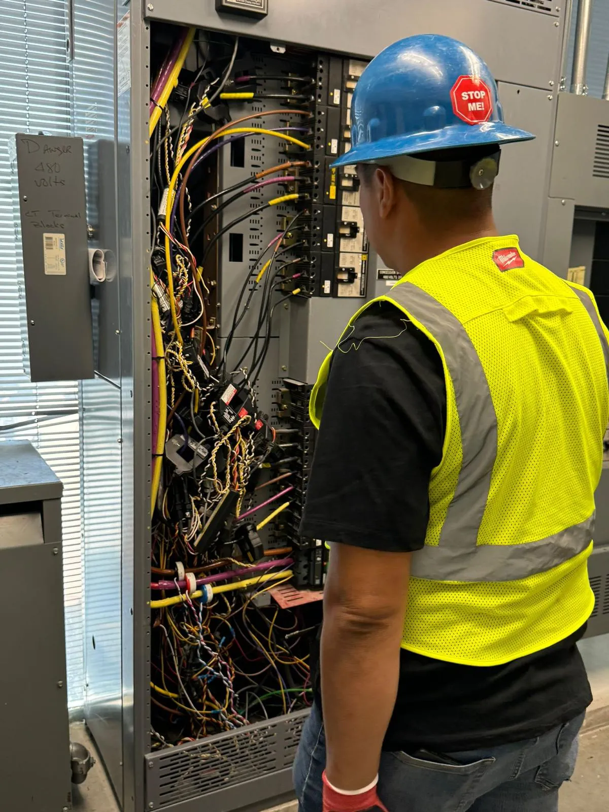 Technician in hard hat inspecting an open 480V commercial panel