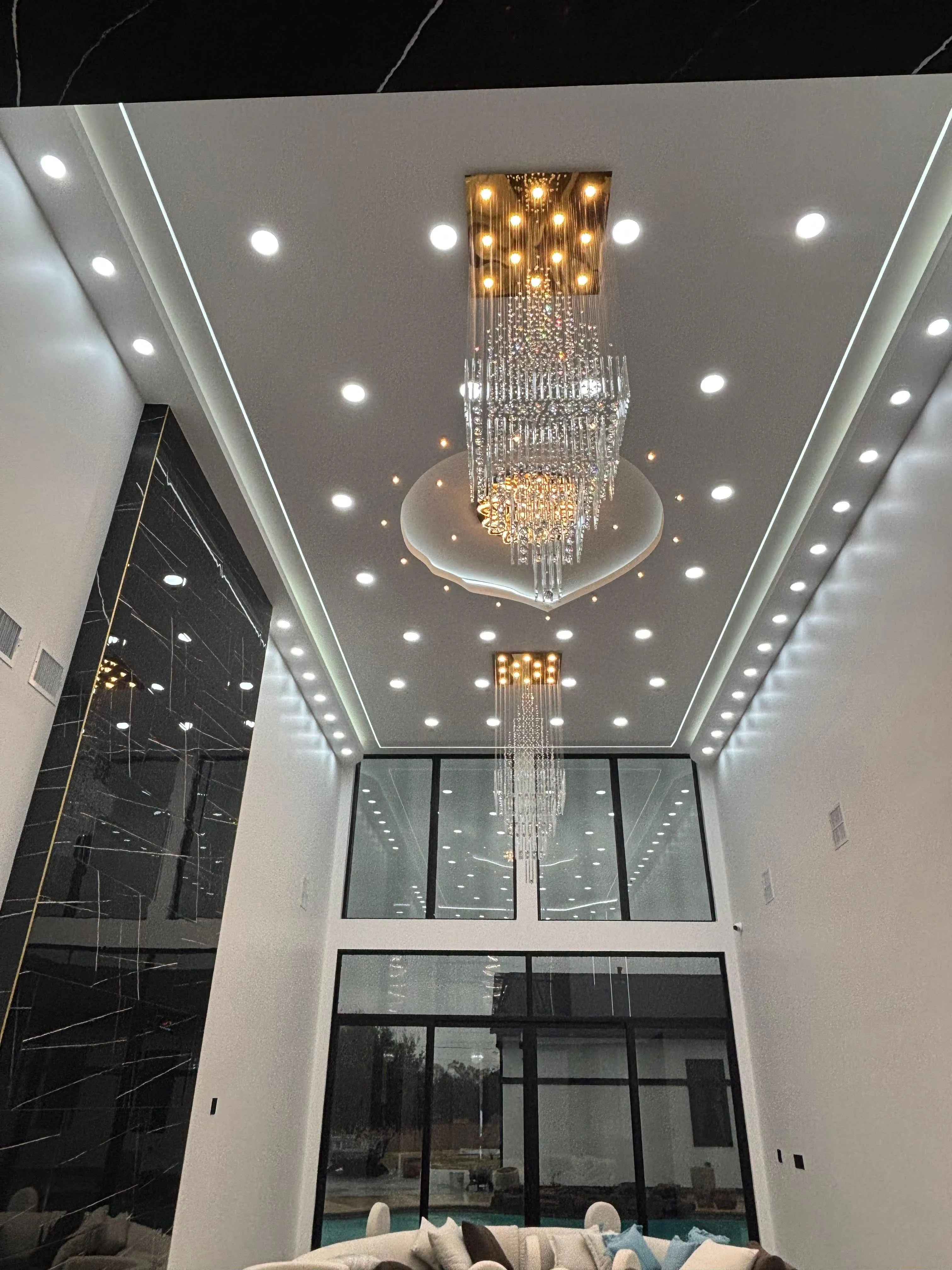 Double-height living room with crystal chandeliers and marble feature wall