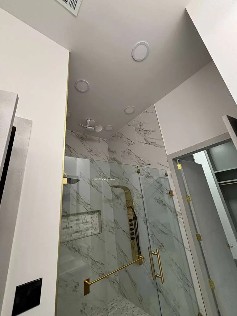 Marble-tiled walk-in shower with gold fixtures and recessed lighting