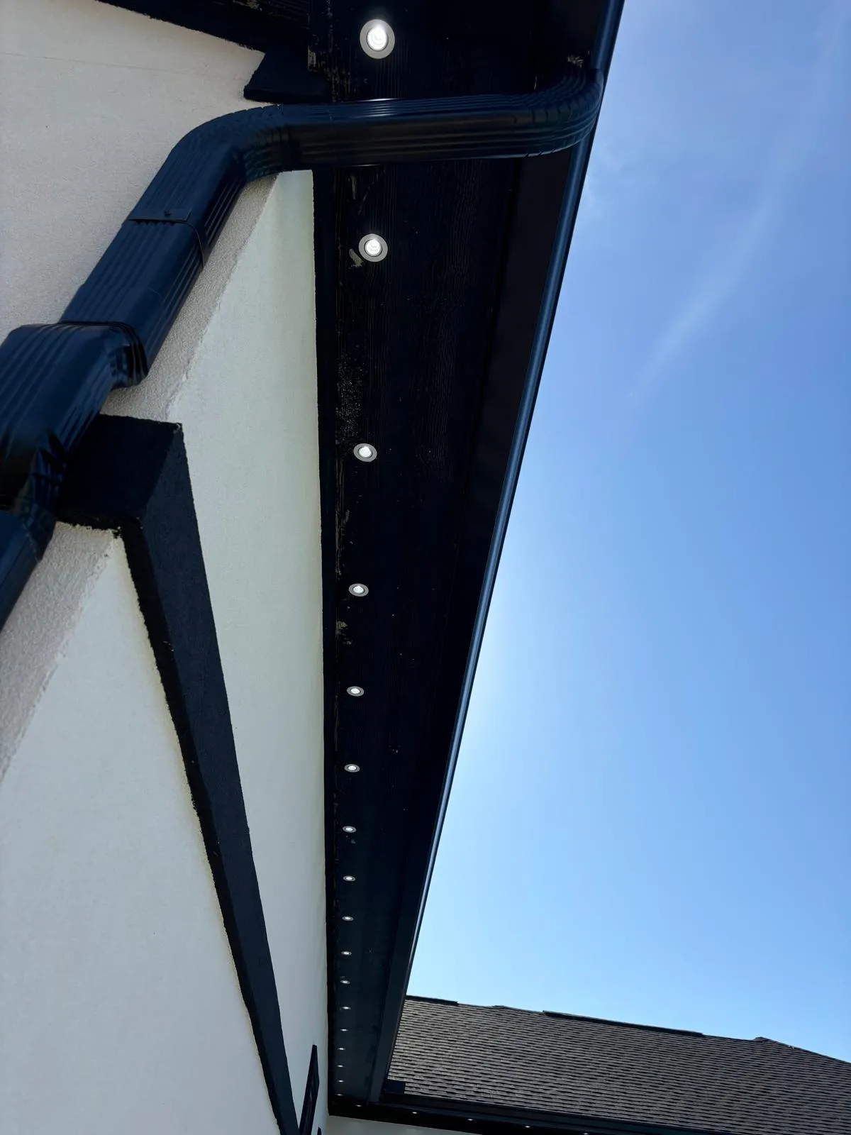 Row of recessed soffit lights along black trim against blue sky