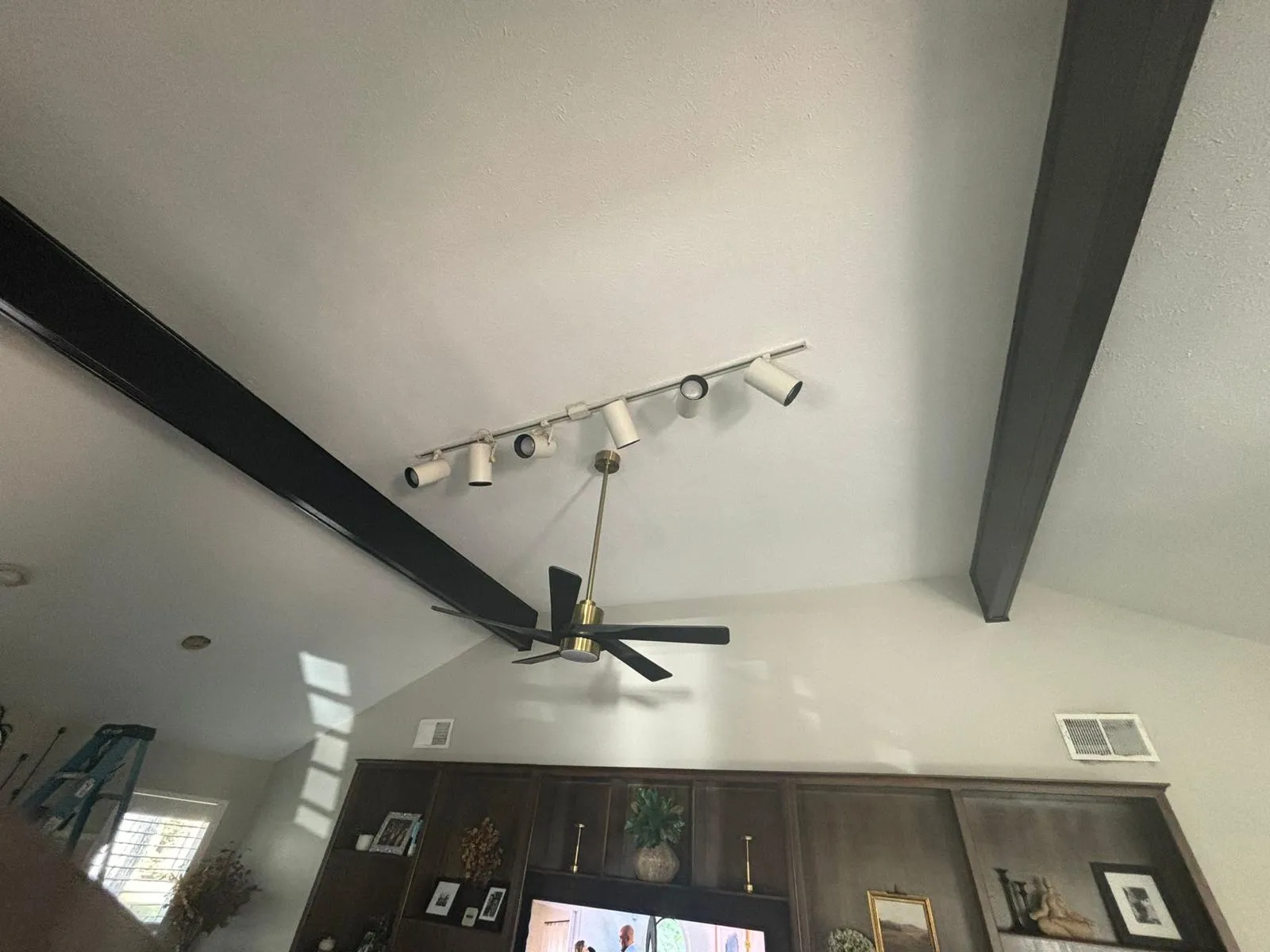 New track lighting and ceiling fan on a vaulted ceiling with black beams
